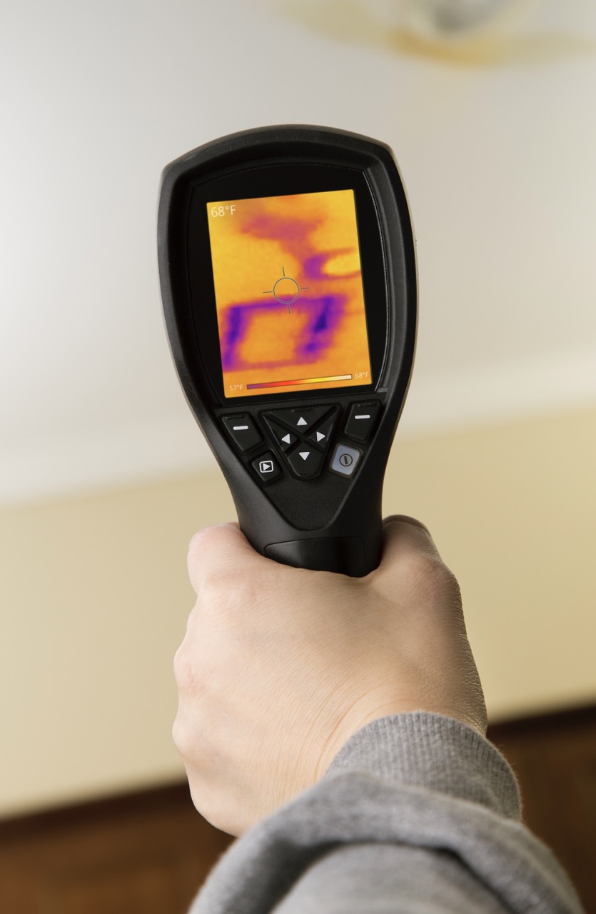 A homes ceiling with a leaking pipe and inspector looking at the damage through a thermal imaging camera